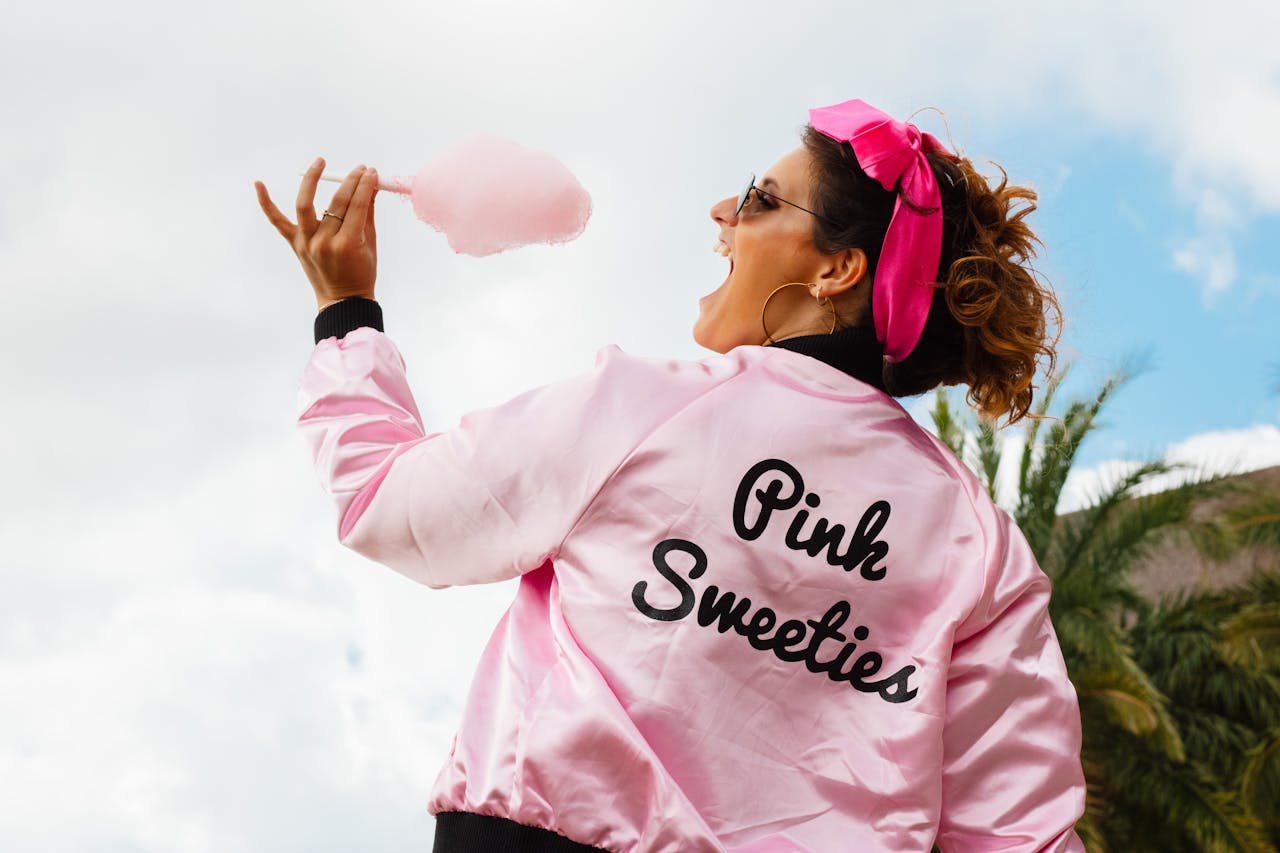 Back view of a woman in a pink jacket holding cotton candy outdoors.