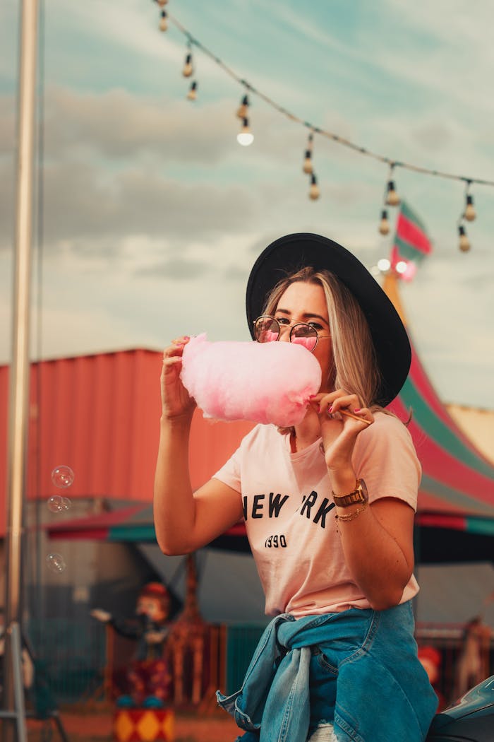 Woman in casual attire savoring cotton candy at a fun carnival setting.
